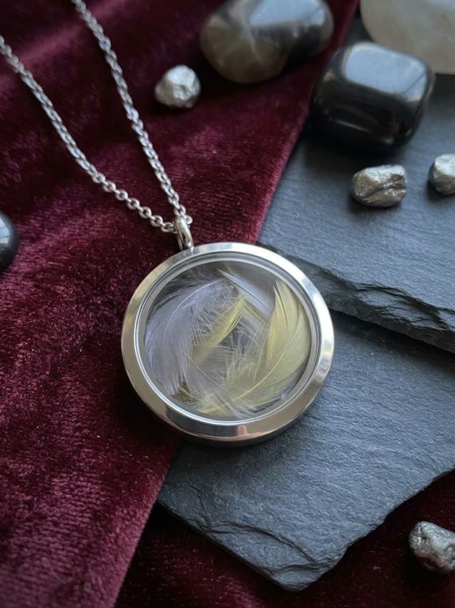 Round glass locket necklace holding grey and yellow cockatiel feathers
